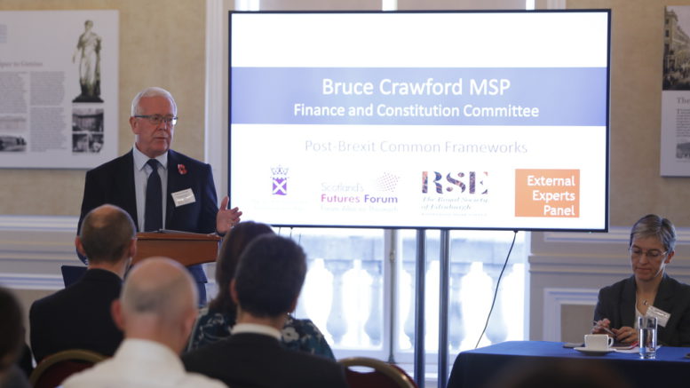 Convener Bruce Crawford MSP stands in front of a screen to introduce the event