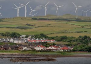 Wind turbines on hills in background with small village down on the shoreline