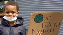 Young boy holding piece of cardboard saying - our futures matter