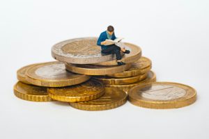 Model of miniature person sitting on Euro coins while reading a book